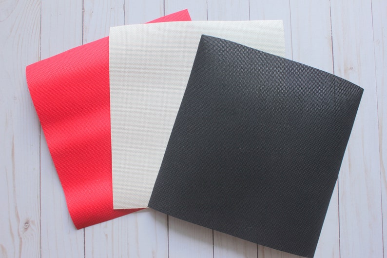 May include: Three fabric swatches, one red, one white, and one black. The swatches are laid out on a white wooden surface.