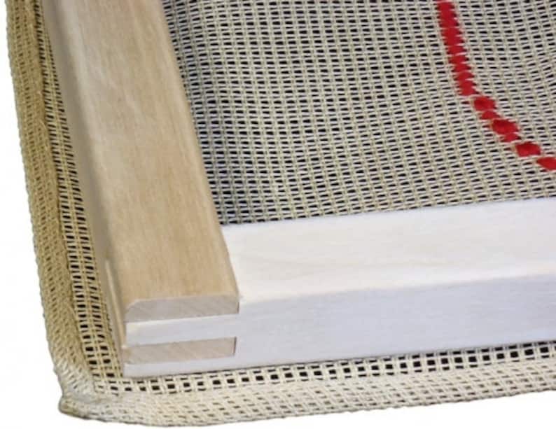 Op de afbeelding: Close-up van een houten borduurring met een witte stof eroverheen gespannen. De stof heeft een rasterpatroon en een rode lijn langs de rand.