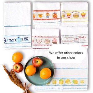 May include: White kitchen towels with embroidered designs. Some towels feature teacups, teapots, and desserts. Others have images of burgers and fries. The image also includes oranges, apples, and a sprig of wheat.