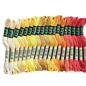 May include: A collection of embroidery floss in a spectrum of warm colors, from cream and yellow to orange and red. Each skein is labeled with a black and green band, and a barcode. Ideal for various craft projects.