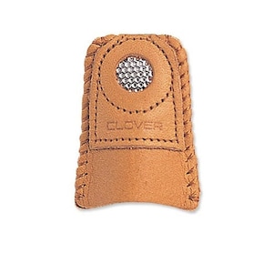 May include: A tan leather thimble with a metal dimpled insert. The thimble has a stitched border and the word "CLOVER" is embossed on the leather. This sewing tool is designed to protect the finger while hand sewing.