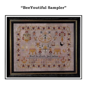 May include: A framed sampler with a light grey background and colourful embroidery. The sampler features a beehive, flowers, a rooster, a windmill, and the text "Don't be afraid, just believe". The alphabet is also embroidered on the sampler.
