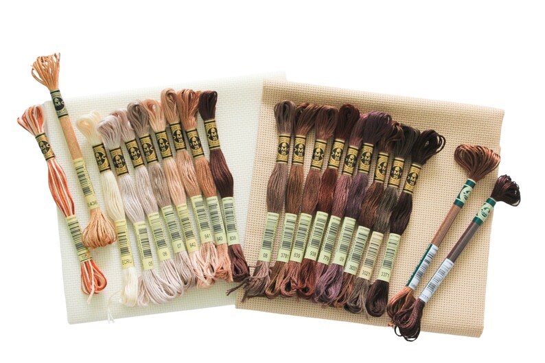 May include: A set of embroidery floss in various shades of brown and beige, arranged on two pieces of Aida cloth. The floss is DMC brand and the colors are numbered.