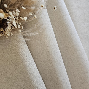 Puede incluir: Primer plano de tela de lino beige con una sutil textura tejida, drapeada en suaves pliegues. Un ramo de flores secas, que incluye margaritas blancas y hierbas beige esponjosas, descansa sobre la tela, añadiendo un toque de elegancia natural. Los tonos neutros crean una estética relajante.