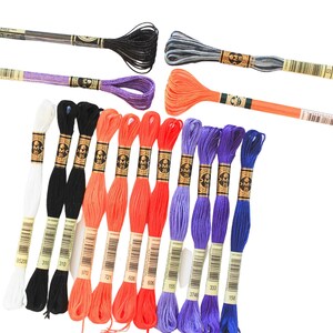 May include: Assortment of embroidery floss spools in various colors, including white, black, orange, purple, and blue. The spools are labeled with DMC numbers.