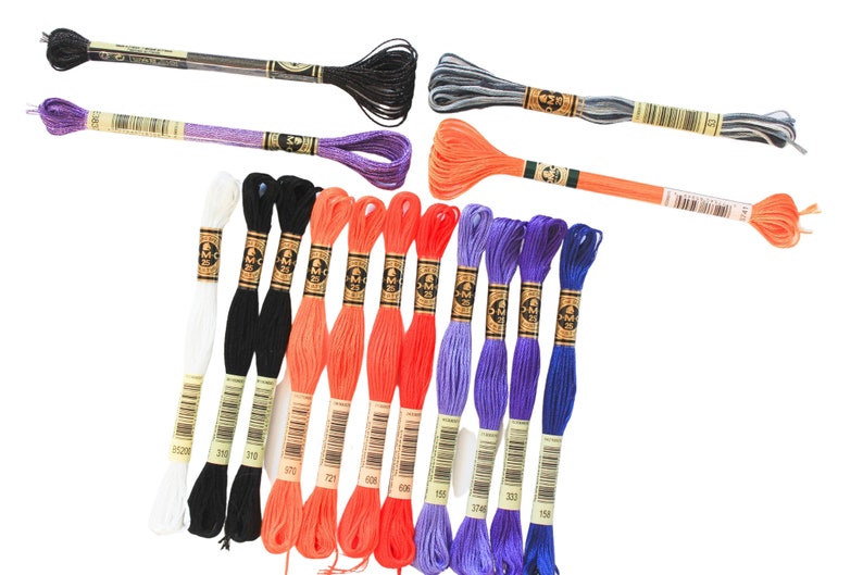 May include: Assortment of embroidery floss spools in various colors, including white, black, orange, purple, and blue. The spools are labeled with DMC numbers.