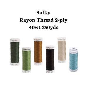Könnte beinhalten: Sechs Spulen Sulky Rayon Garn 2-fädig 40wt 250yds in verschiedenen Farben: Grün, Olivgrün, Braun, Schwarz, Beige und Blau.