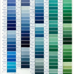 May include: DMC embroidery floss color chart with a range of blues and greens. Each color is numbered and displayed in a vertical column. The chart includes a DMC logo and text indicating the thread's compliance with safety standards.