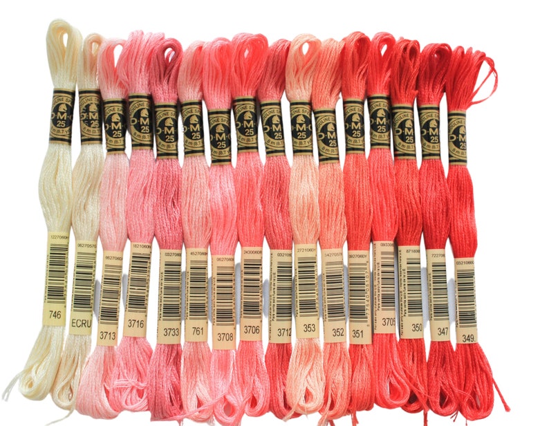 May include: A set of 16 embroidery floss spools in shades of pink, red, and white. The spools are labeled with DMC numbers and the colors range from a pale cream to a bright red.