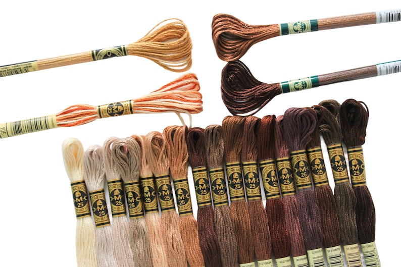May include: A collection of DMC embroidery floss in various shades of brown, beige, and cream. The floss is wound on spools with the DMC logo and number.