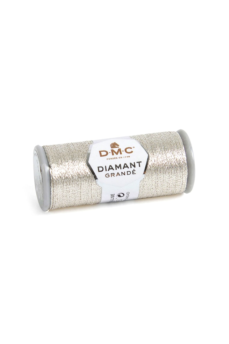 May include: A silver metallic DMC Diamant Grand&eacute; thread spool. The thread is wrapped around a gray plastic spool. The label reads "DMC Diamant Grand&eacute;". This thread is ideal for embroidery and decorative stitching projects.