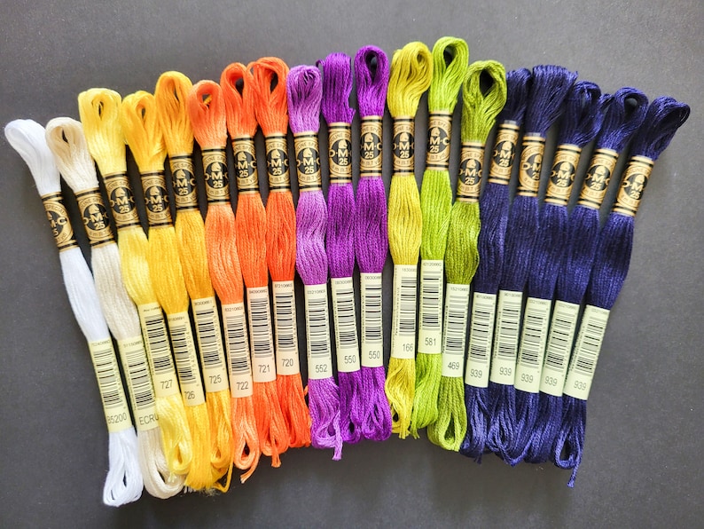 Peut inclure: Assortiment de bobines de fil &agrave; broder DMC de diff&eacute;rentes couleurs, notamment blanc, jaune, orange, violet, vert et bleu. Les bobines sont &eacute;tiquet&eacute;es avec les num&eacute;ros DMC, notamment 727, 725, 722, 552, 550, 168, 581, 469, 606, 906, 939, 539 et 909.