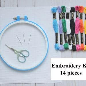 May include: Embroidery kit containing 14 pieces, including a blue embroidery hoop, white Aida fabric, three embroidery needles, a pair of scissors, and eight spools of floss in various colours.