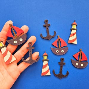 Puede incluir: Una colección de adornos de madera con temática náutica, que incluyen veleros, faros y ancres. Los adornos están pintados en rojo, blanco y azul.