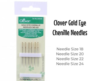 Może przedstawiać: Opakowanie igieł chenille Clover Gold Eye w rozmiarach 18, 20, 22 i 24. Igły mają złote oczka i są zapakowane w biało-zielone opakowanie z logo Clover.