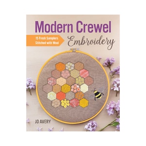 May include: Book cover featuring a close-up of a beige embroidery hoop with a honeycomb design in shades of yellow, orange, and red. The embroidery is surrounded by purple flowers and a small bee. The title of the book is "Modern Crewel Embroidery" with the subtitle "15 Fresh Samplers Stitched with Wool". The author's name, "JO AVERY", is printed at the bottom of the cover.