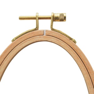 May include: A wooden embroidery hoop with a brass screw tightening mechanism. The hoop is made of two concentric rings, and the inner ring is slightly smaller than the outer ring.