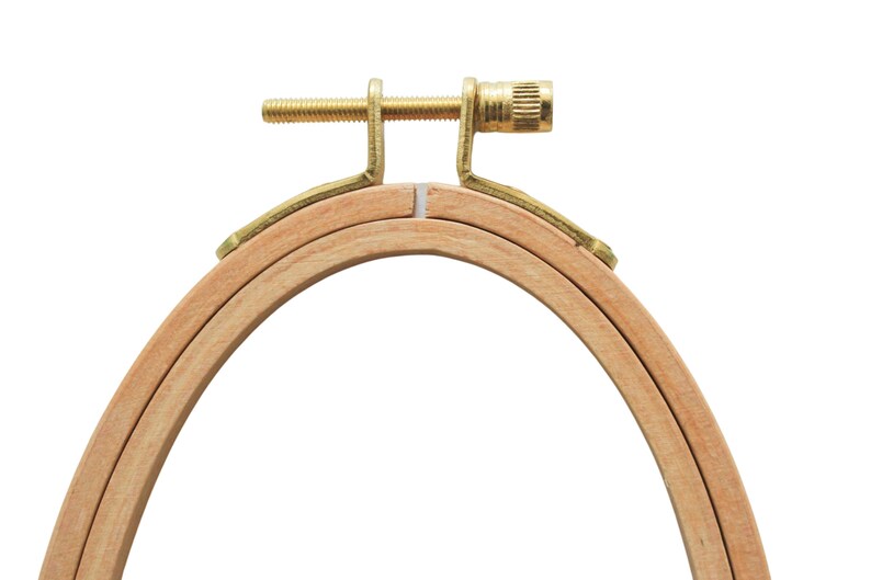 May include: A wooden embroidery hoop with a brass screw tightening mechanism. The hoop is made of two concentric rings, and the inner ring is slightly smaller than the outer ring.