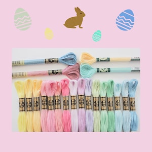 May include: A collection of colorful embroidery floss in various pastel shades, including yellow, pink, blue, and green. The floss is arranged on a white surface, with Easter-themed illustrations of eggs and a bunny in the background.