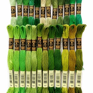 May include: A collection of twenty-three DMC embroidery floss skeins in various shades of green, ranging from light lime to deep forest and olive tones. Each skein features a gold and black paper label with the text DMC 25 and 8.7 yards.