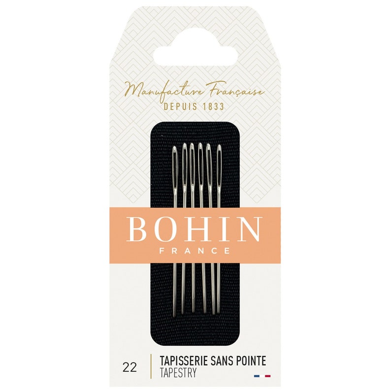 以下が含まれることがあります： Bohin Franceのタペストリー針のパッケージ。パッケージは、"Manufacture Fran&ccedil;aise Depuis 1833"と"BOHIN FRANCE"のテキストが入った白とピーチ色の背景です。6本の銀色の針が黒い背景に表示されています。"TAPISSERIE SANS POINTE TAPESTRY"のテキストも表示されています。