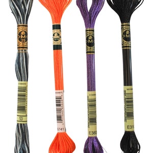 May include: Four spools of DMC embroidery floss in black, orange, purple, and a silver and black variegated color. The spools are labeled with the DMC color numbers and names: 302106 E31, 233057L S741, 513000 E383, and 5130057H 53.
