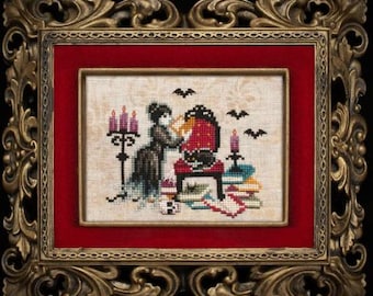 May include: Cross-stitch artwork in an ornate gold frame. The framed piece depicts a gothic scene with a woman, a red chair, candles, bats, and a skull. The artwork is framed with a red mat.