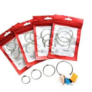 May include: Four red resealable plastic pouches containing silver metal rings, with additional loose silver metal rings and three small spools of thread in light pink, blue, and yellow arranged in front of the pouches on a white background.