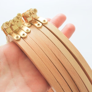 May include: A set of six wooden embroidery hoops with brass screw closures. The hoops are stacked on top of each other, with the largest hoop at the bottom and the smallest hoop at the top.