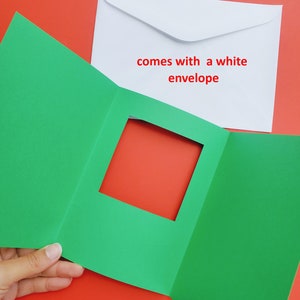 May include: A green card with a square window cut out. The card is folded in thirds. The card comes with a white envelope. The text on the envelope reads "comes with a white envelope".