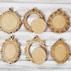 May include: Six unfinished wooden frames in various ornate shapes, including round and oval designs. Each frame has a small hole at the top for hanging. The frames are made of light brown wood and are arranged on a white wooden surface.