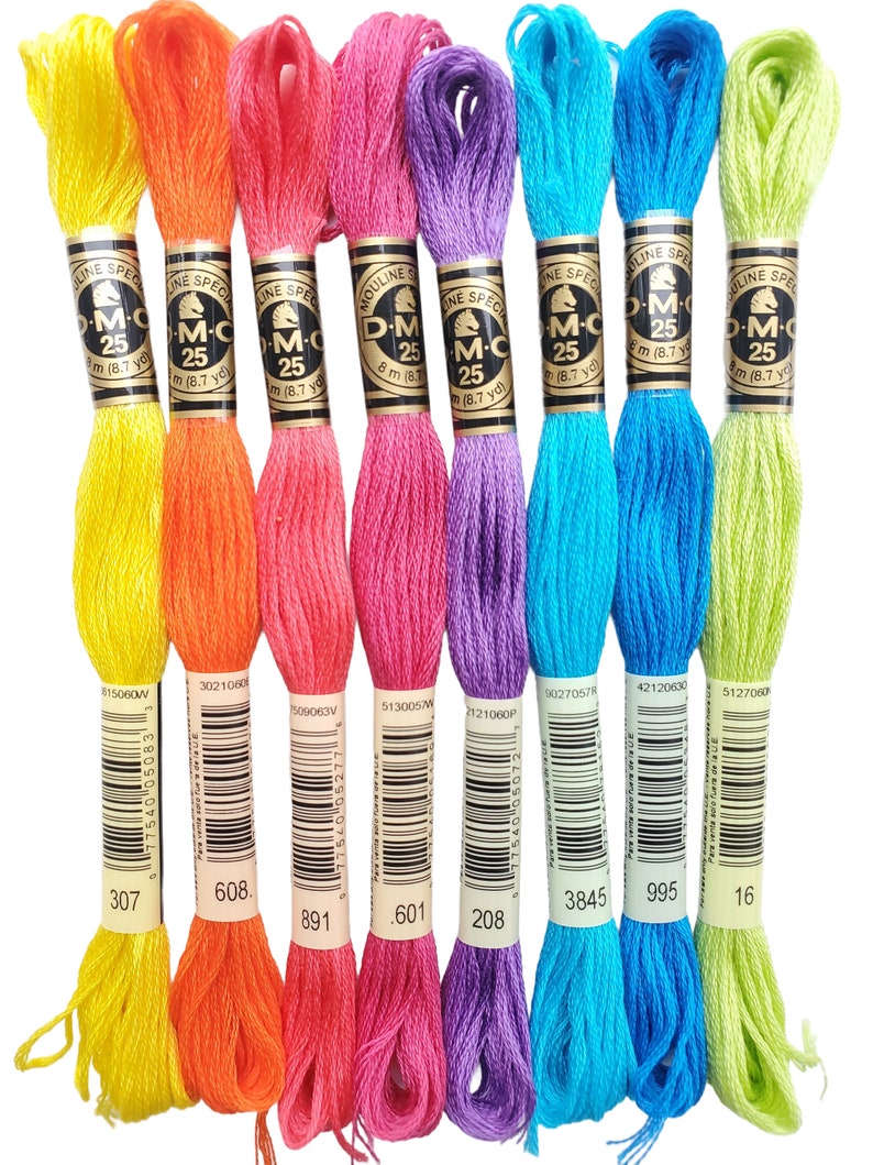 K&ouml;nnte beinhalten: Acht Spulen DMC Stickgarn in verschiedenen Farben, darunter Gelb, Orange, Rosa, Lila, Blau und Gr&uuml;n. Jede Spule hat ein schwarzes Etikett mit dem DMC-Logo und der Nummer der Farbe. Die Nummern sind 307, 608, 891, 601, 208, 3845, 995 und 16.