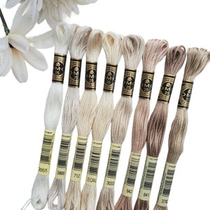 Peut inclure: Huit bobines de fil à broder DMC dans différentes nuances de blanc et de beige. Les bobines sont étiquetées avec les numéros de couleur DMC : 3865, 3866, 712, ECRU, 3033, 842, 841 et 3780.