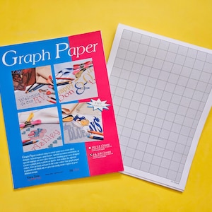 May include: A blue and pink pamphlet titled "Graph Paper" with a grid pattern on the cover. The pamphlet is next to a sheet of graph paper with a black grid pattern.