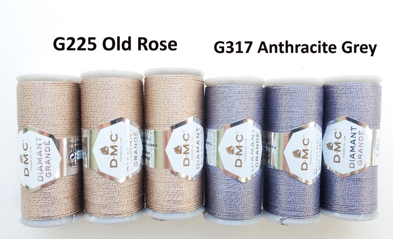 May include: Six spools of DMC Diamant Grande thread in two colors: G225 Old Rose and G317 Anthracite Grey. The thread is wound on white spools with silver labels. The Old Rose thread is a light, shimmering pink, while the Anthracite Grey is a dark, metallic gray.