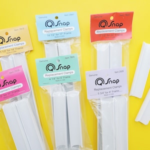 May include: Six packages of white plastic replacement clamps for picture frames. Each package has a different size and is labeled with the QSnap logo and the size of the frame it fits. The packages are on a yellow background.
