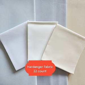 Könnte beinhalten: Drei Stücke weißen Hardanger-Stoffes, eines in einem hellblauen Farbton, eines in einem weißen Farbton und eines in einem cremefarbenen Farbton. Der Stoff ist 22-fädig.