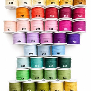 May include: A collection of 4mm spools of thread in various colors arranged in a grid. Each spool is labeled with a specific numerical code, including 501, 700, 655, 666, 511, 668, 705, 512, 524, 563, 707, 537, 540, 204, 565, 566, 568, 024, 574, 517, 601, 703, 600, 012, 585, 607, 625, 617, 702, 706, 618, 629, 240, 633, 653, 651, 656, 648, 671, 704, and 002.
