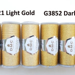May include: Six spools of DMC Diamant Grande metallic thread in light gold (G3821) and dark gold (G3852). Each spool is wrapped with a silver and white label. The thread is a shiny, golden color, perfect for embroidery and other crafts.