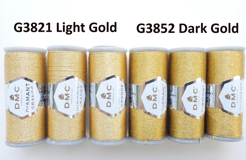 May include: Six spools of DMC Diamant Grande metallic thread in light gold (G3821) and dark gold (G3852). Each spool is wrapped with a silver and white label. The thread is a shiny, golden color, perfect for embroidery and other crafts.