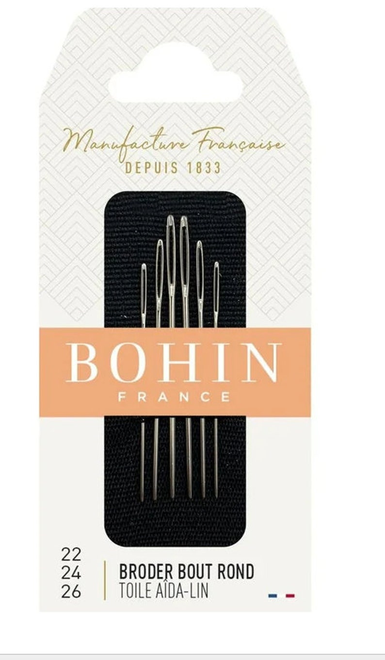 以下が含まれることがあります： Bohin Franceの刺繍針のパッケージ。パッケージは白とタンのデザインで、「Manufacture Fran&ccedil;aise DEPUIS 1833」と「BOHIN FRANCE」の文字が入っています。針は銀色で、「BRODER BOUT ROND TOILE AIDA-LIN」と表示されています。