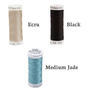 Puede incluir: Tres carretes de hilo, uno en color crudo, uno en negro y uno en verde jade medio. Los carretes est&aacute;n etiquetados con el nombre de la marca "Sulky" y el peso del hilo "40wt".