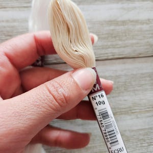 May include: Close-up of two spools of embroidery thread. One spool is white, and the other is ecru. The ecru spool is labeled "N&deg;16 10g" and "ECRU". The text "4 non-divisible strands in size 16 thread" is also visible.