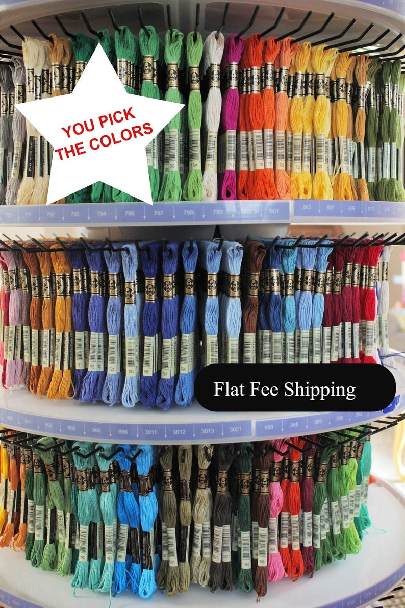 May include: A display of colorful embroidery floss in various shades, including green, blue, orange, and pink. The text "YOU PICK THE COLORS" is visible. The floss is organized on a tiered, circular rack.