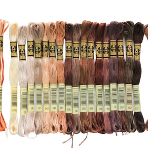 May include: A collection of 20 DMC embroidery floss spools in shades of brown, beige, and orange. The spools are arranged in a row, with the numbers 436, 105, ECRU, 05, 06, 07, 842, 841, 843, 838, 08, 3781, 839, 771, 09, 3031, 3021, 3371 visible on the labels.