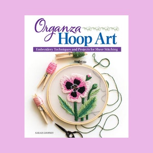 May include: A book titled "Organza Hoop Art: Embroidery Techniques and Projects for Sheer Stitching" by Sarah Godfrey. The cover features a close-up of a hoop with a pink and green embroidered flower.