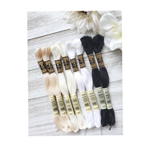 May include: A collection of ten embroidery floss spools in various shades of white and black. The spools are labeled with the DMC color numbers: ECRU, ECRU, 3865, 3865, 85200, 85200, 310, 310.