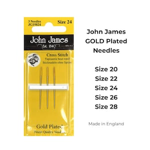 May include: A pack of three gold-plated cross stitch needles, size 24, by John James, Est. 1840. The needles are packaged on a yellow card with the brand name and size printed on it. The package also includes the text "Cross Stitch", "Tapisserie bout rond", and "Sticknadeln ohne Spitze".