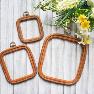 May include: Three wooden embroidery hoops of different sizes, with a brown finish. The hoops are on a white wooden background.
