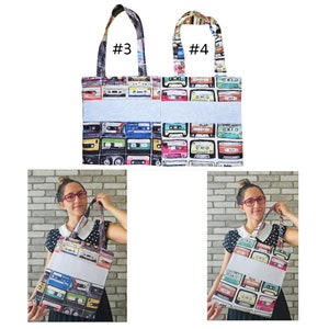 May include: Two tote bags with a white background and a colorful pattern of cassette tapes. The bags have a light blue stripe across the middle. The bags are labeled #3 and #4. Two people are holding the bags in the image.